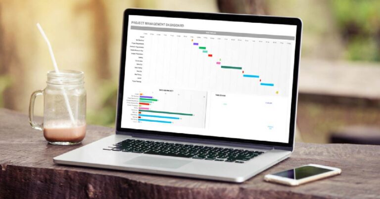 Laptop on a wooden desk with coffee cup, showing Excel for Small Business balance sheet, bar chart of total assets, and line graph of asset predictions — illustrating how spreadsheets simplify financial tracking for small business owners.