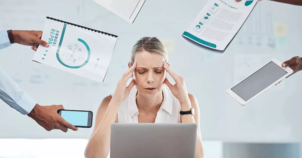 Stressed business owner sitting at a desk with a laptop, surrounded by hands offering documents, devices, and charts — symbolizing the urgent need for Virtual Business Support to manage overwhelm and multitasking.